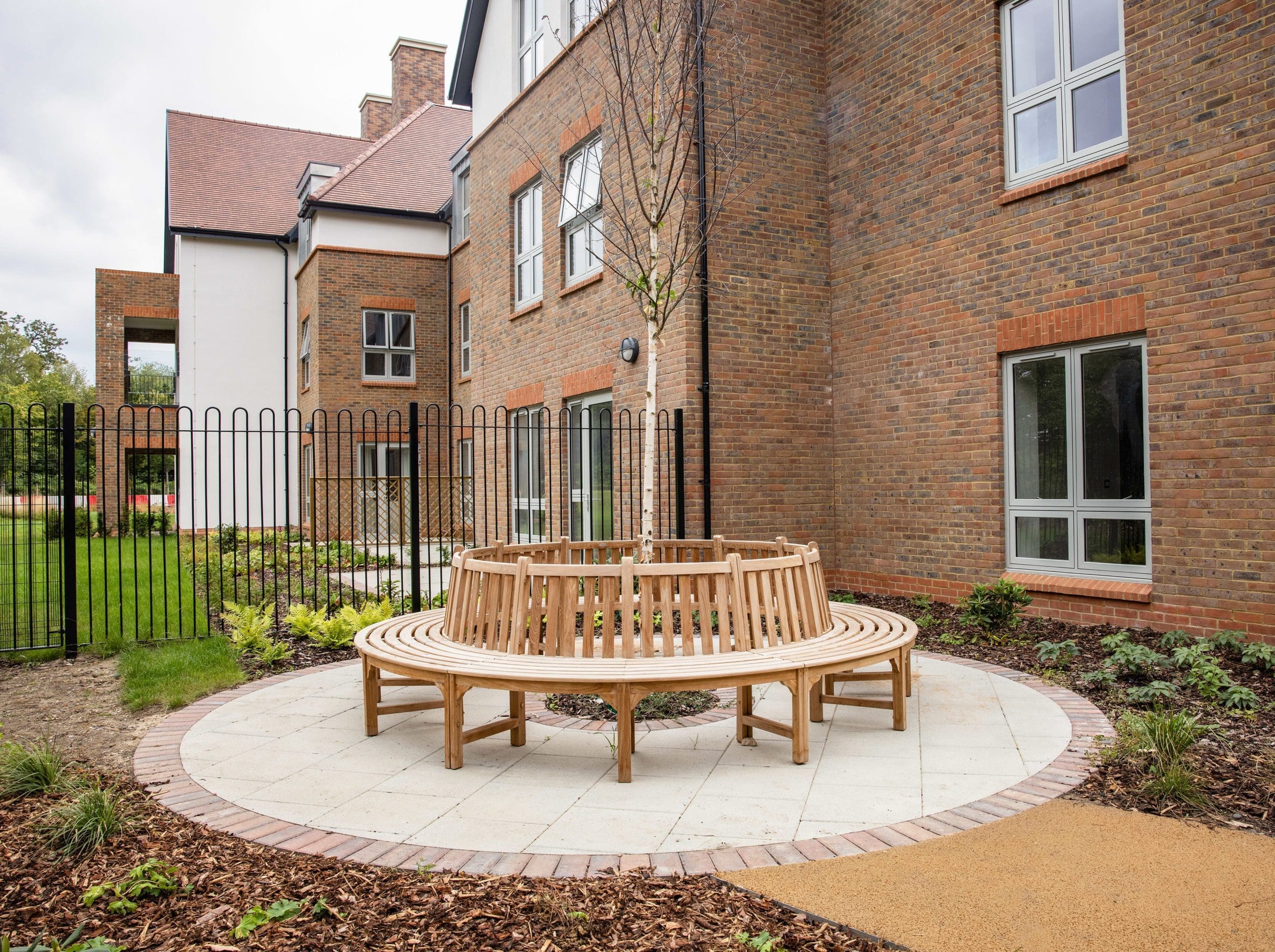 Connected circle of traditional wooden park benches surrounding small tree