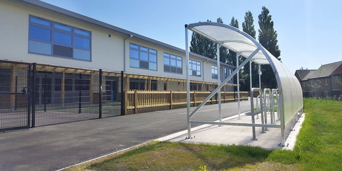 Outdoor curved metal bicycle shelter with transparent plastic cover infront of school gates