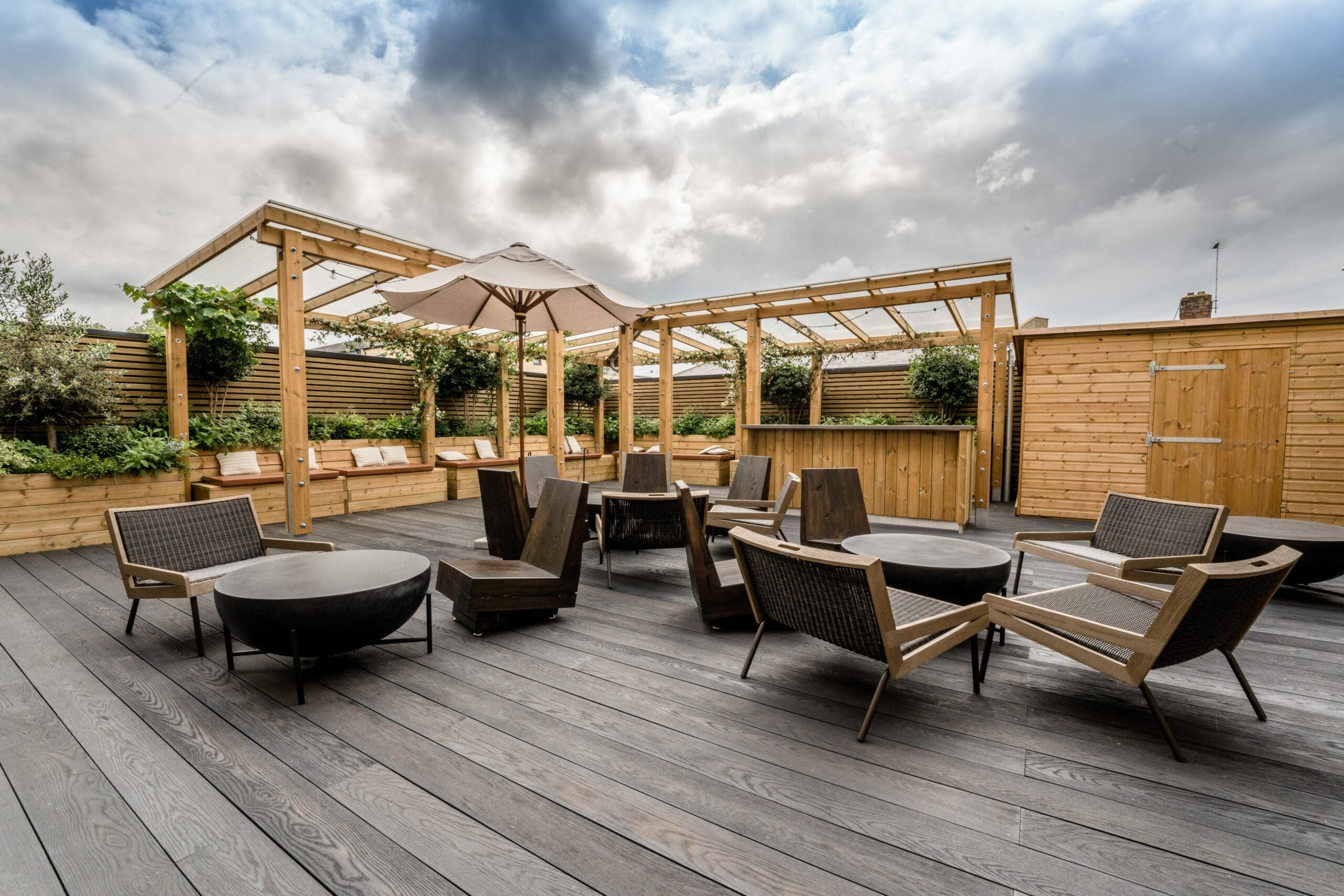 wide shot of wooden bespoke pergolas with built in benches in the background and other outdoor furniture in the foreground