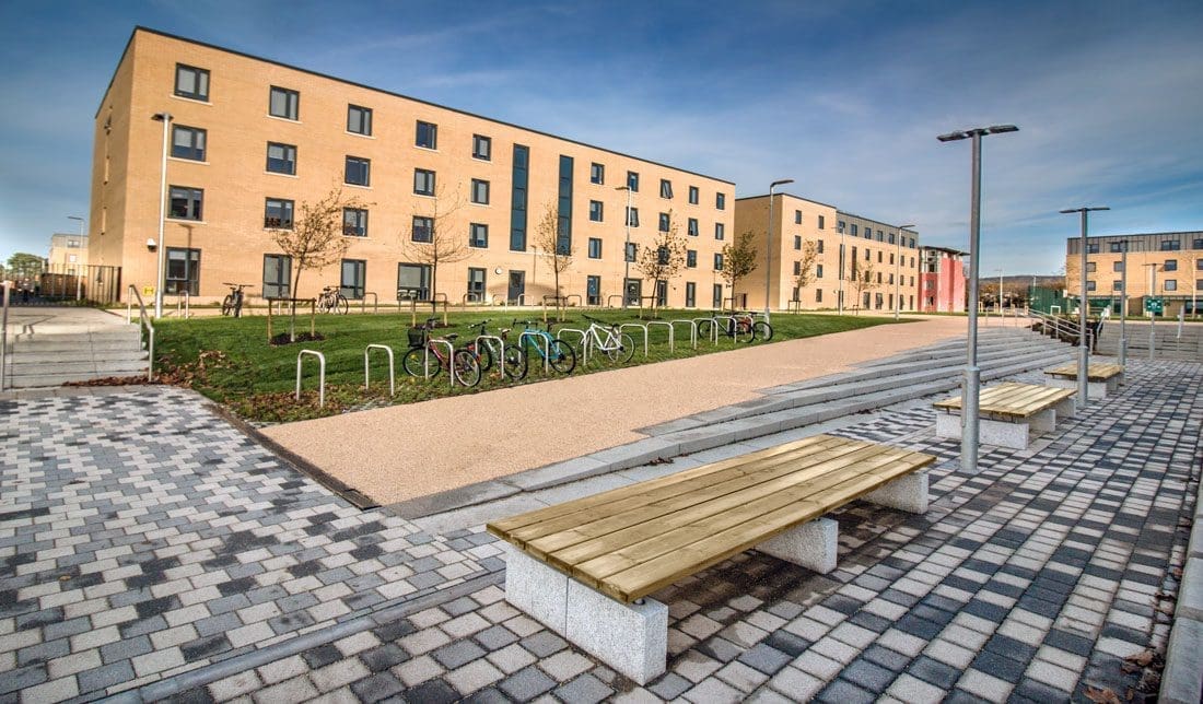 Row of double width outdoor benches wooden topped with concrete plinth legs outside university building