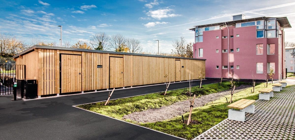 Long outdoor bicycle storage unit next to pink university buildings
