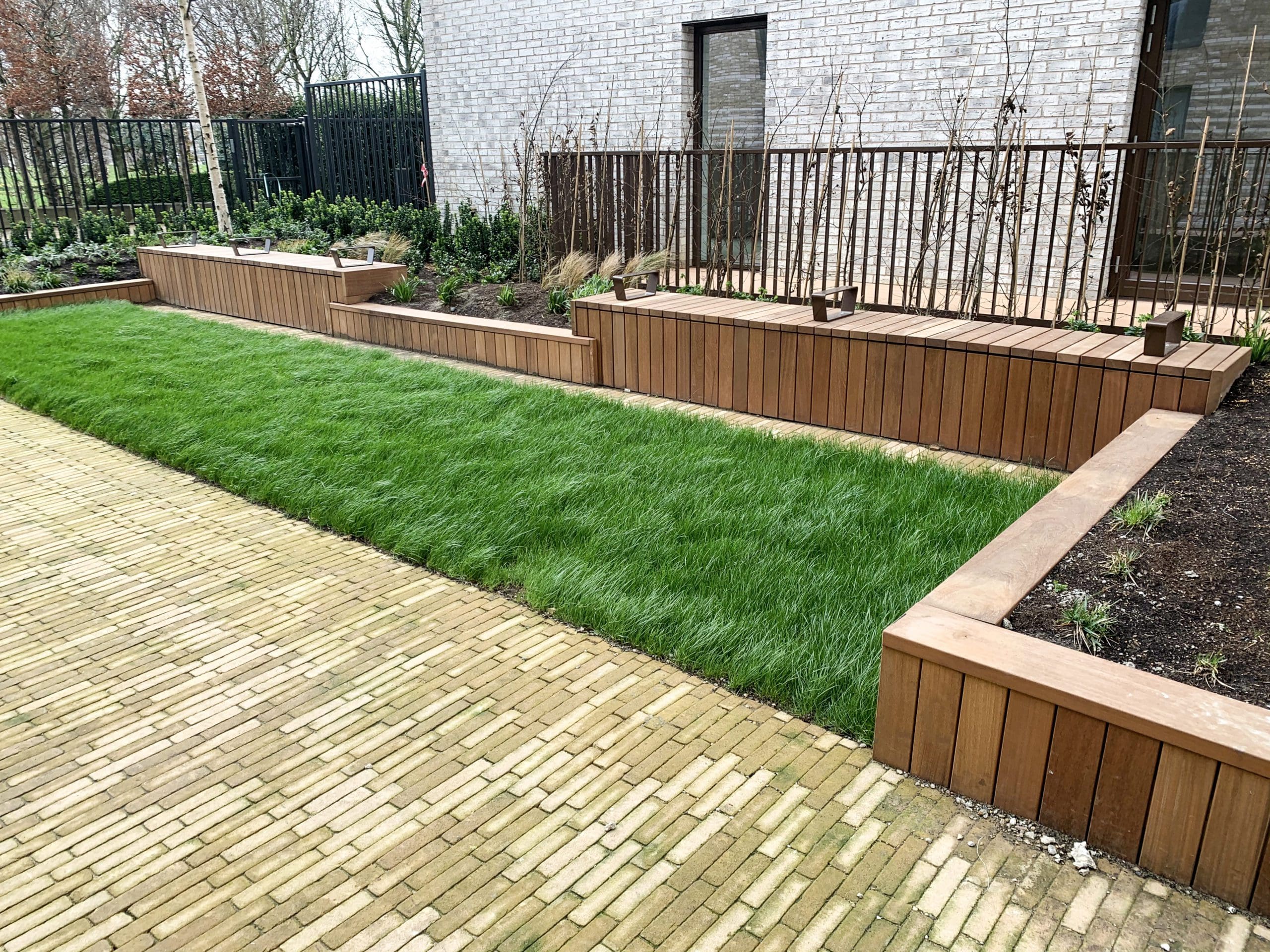 Angled line of wooden timber seating bench with arm rest separators in between raised bed planters