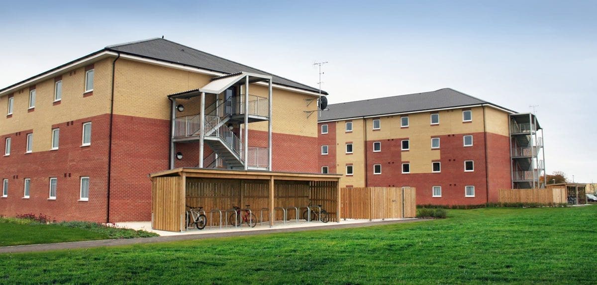 Outdoor open side wooden bicycle shelter with row of bicycle storage hoops and fill of bikes