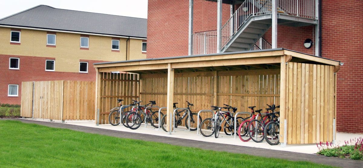 Outdoor open side wooden bicycle shelter with row of bicycle storage hoops and fill of bikes