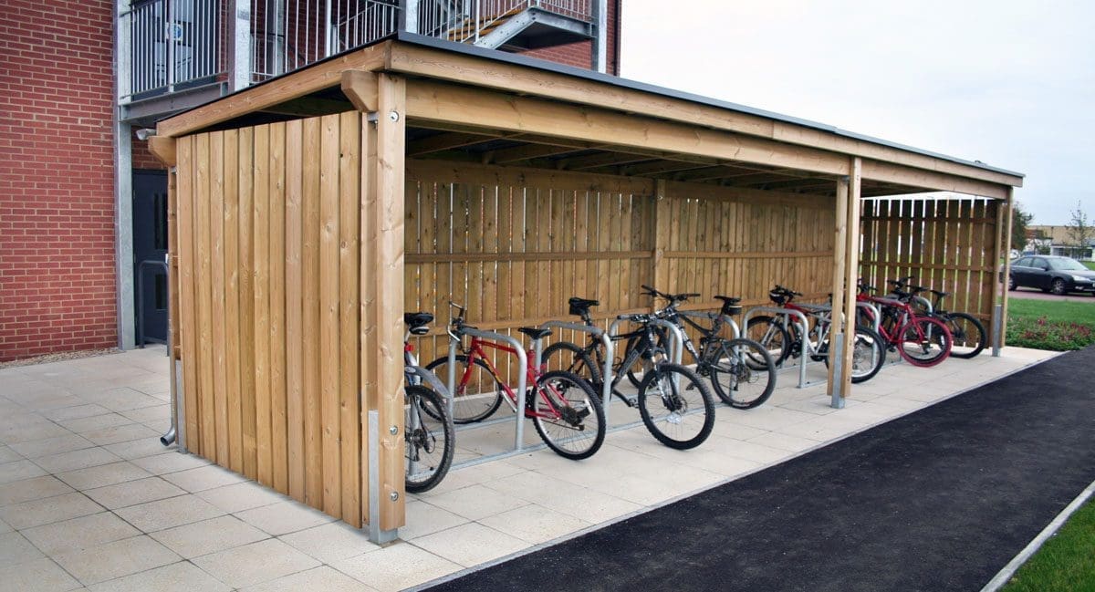 Outdoor open side wooden bicycle shelter with row of bicycle storage hoops and fill of bikes