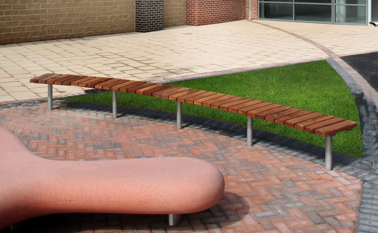 Curved semi circle woods slatted bench with metal legs and green grass behind it