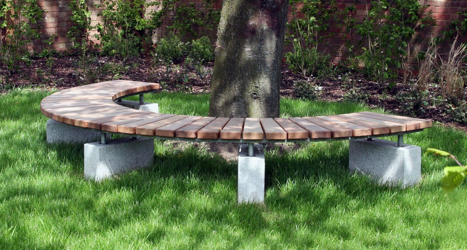 Wooden semicircle bench with concrete plinth legs around tree in grass