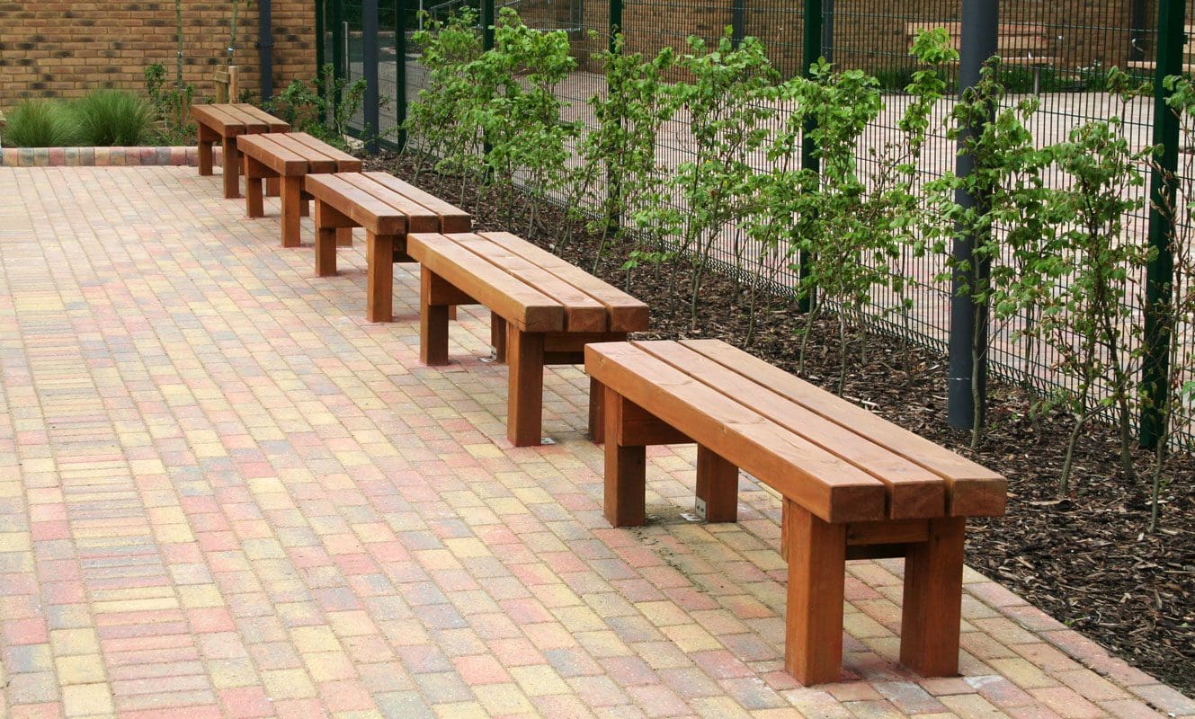Collection of straight wooden benches in a row infront of bushes
