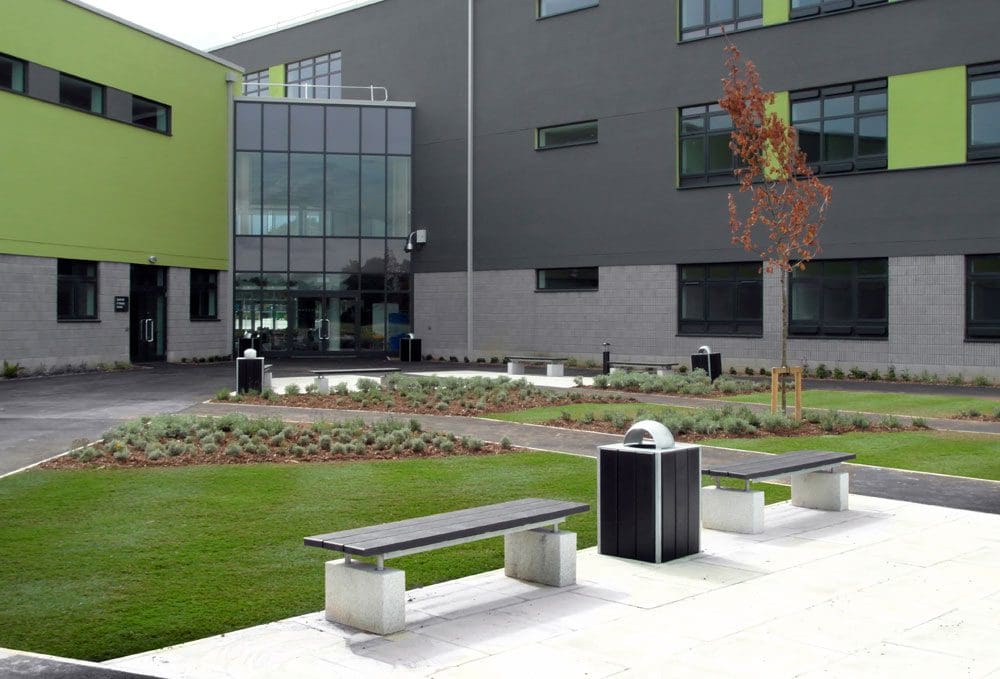 Exterior shot of school showing outdoor black wooden benches with concrete plinth legs and black wood and metal bins