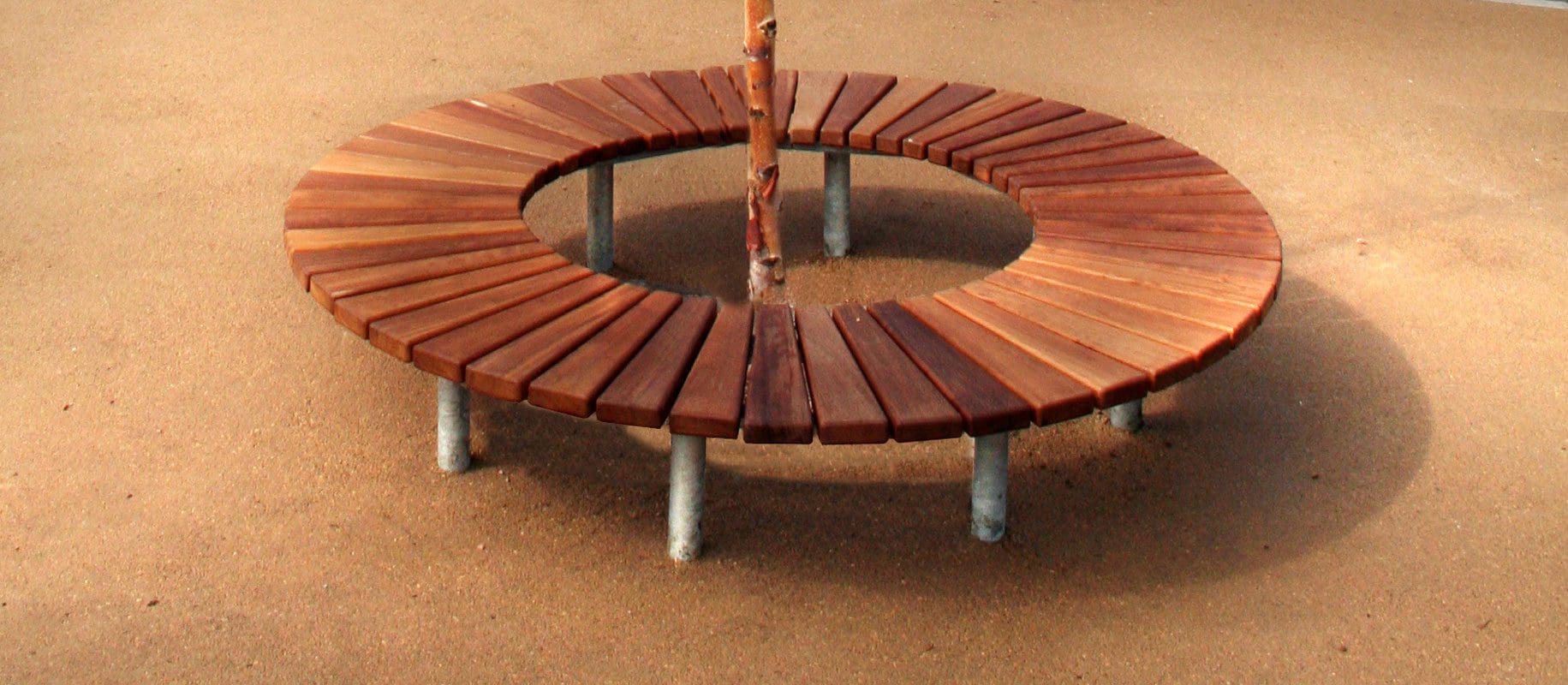 Wooden slatted circle bench with metal legs surrounding small tree