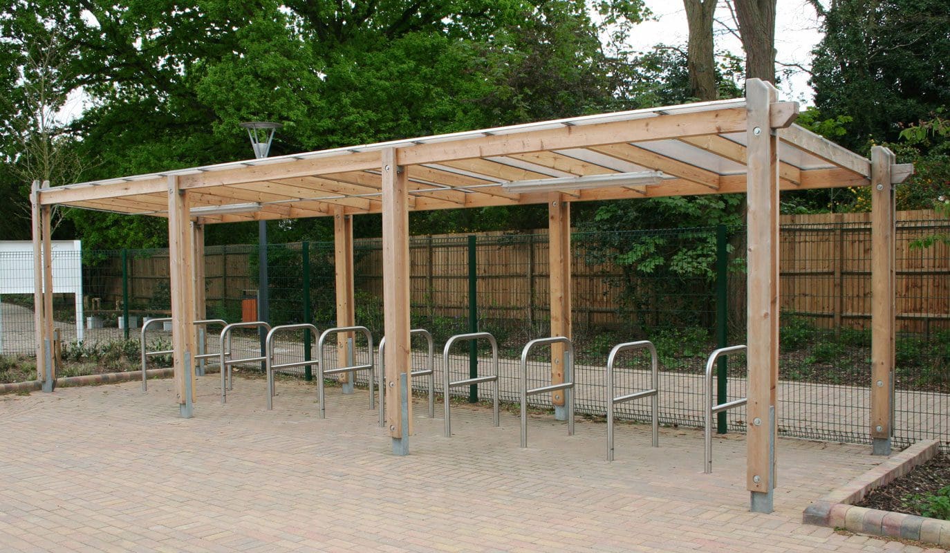 Line of outdoor metal bike hoops under wooden pergola shelter