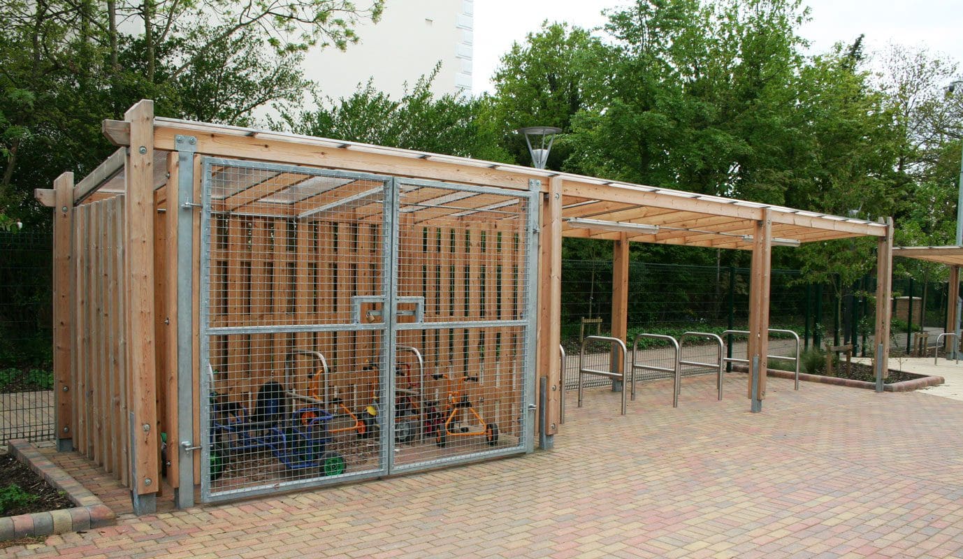 Line of outdoor metal bike hoops under wooden pergola shelter with attached enclosed bike shelter
