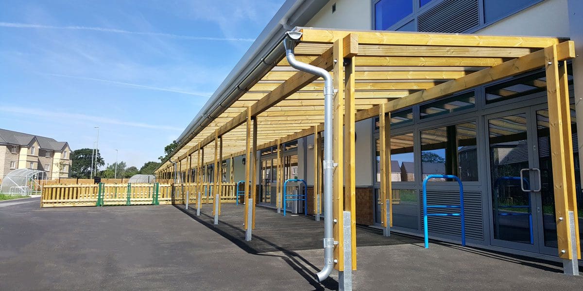 Long wooden pergola attached to school with metal drainage