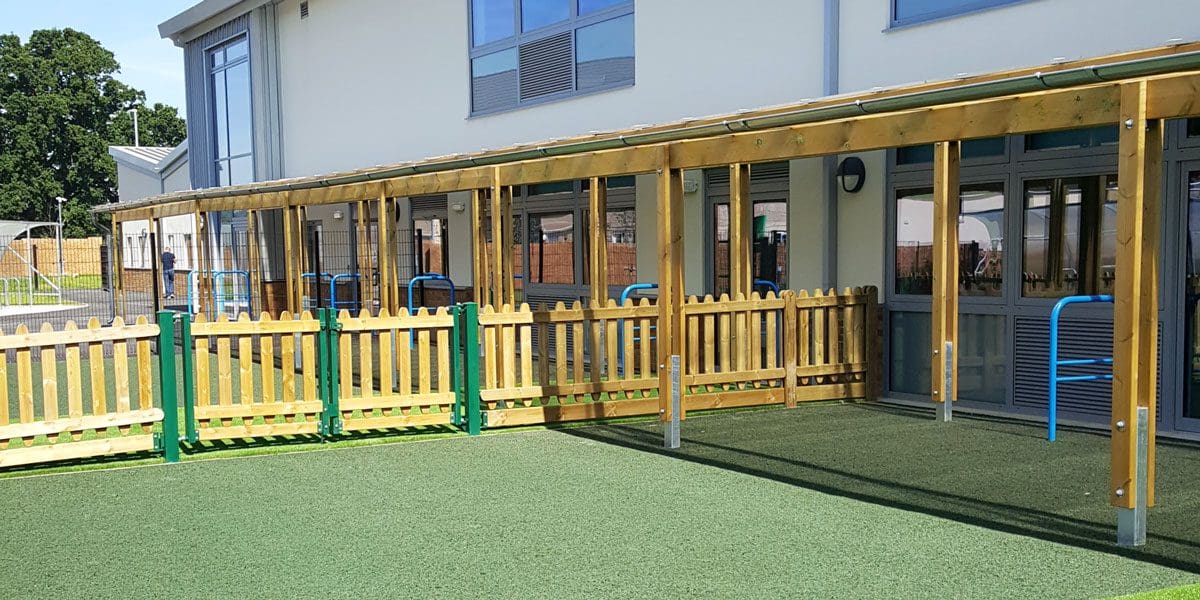 Long wooden pergola attached to school with surrounding wooden 3m tall fence