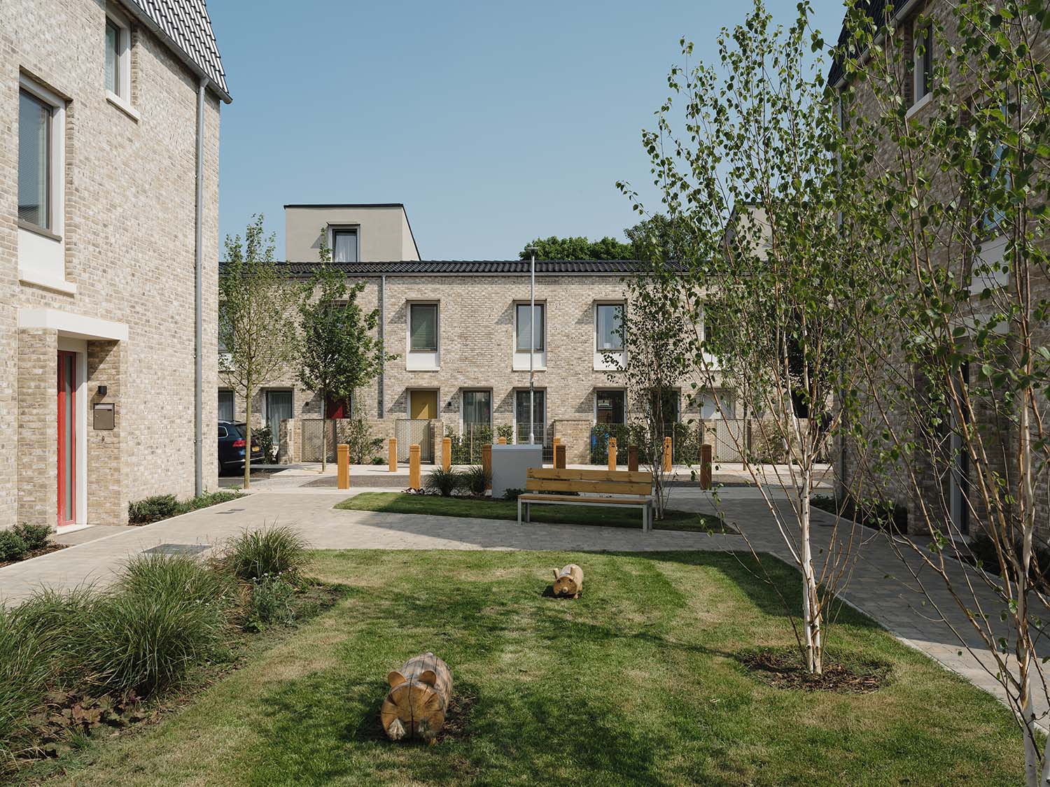 Outdoor communal garden area with wooden parking bollard, grass and wooden park benches with metal legs