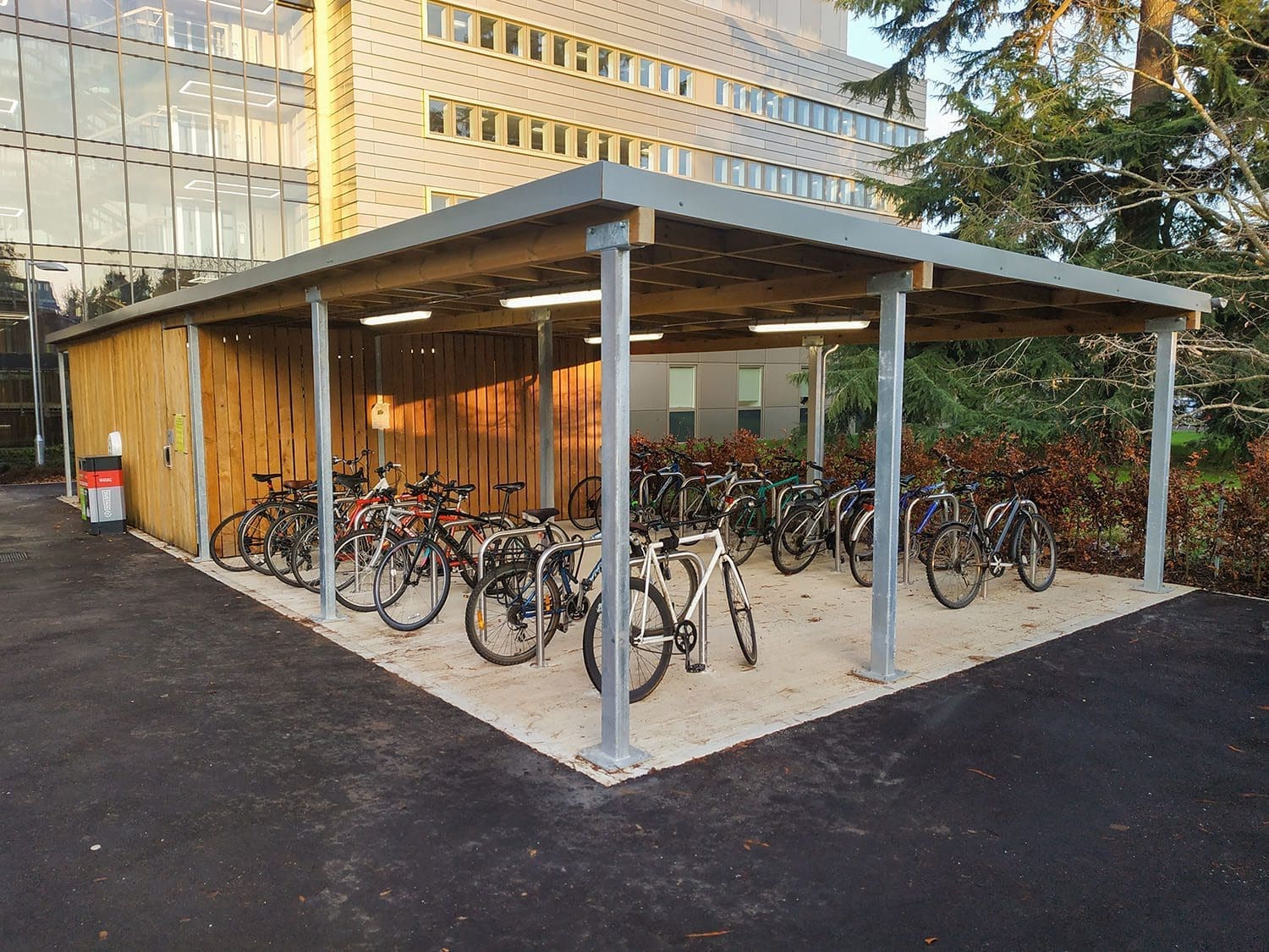 Rows of metal bike secure hoops under wooden and metal canopy connected to outdoor wooden storage area
