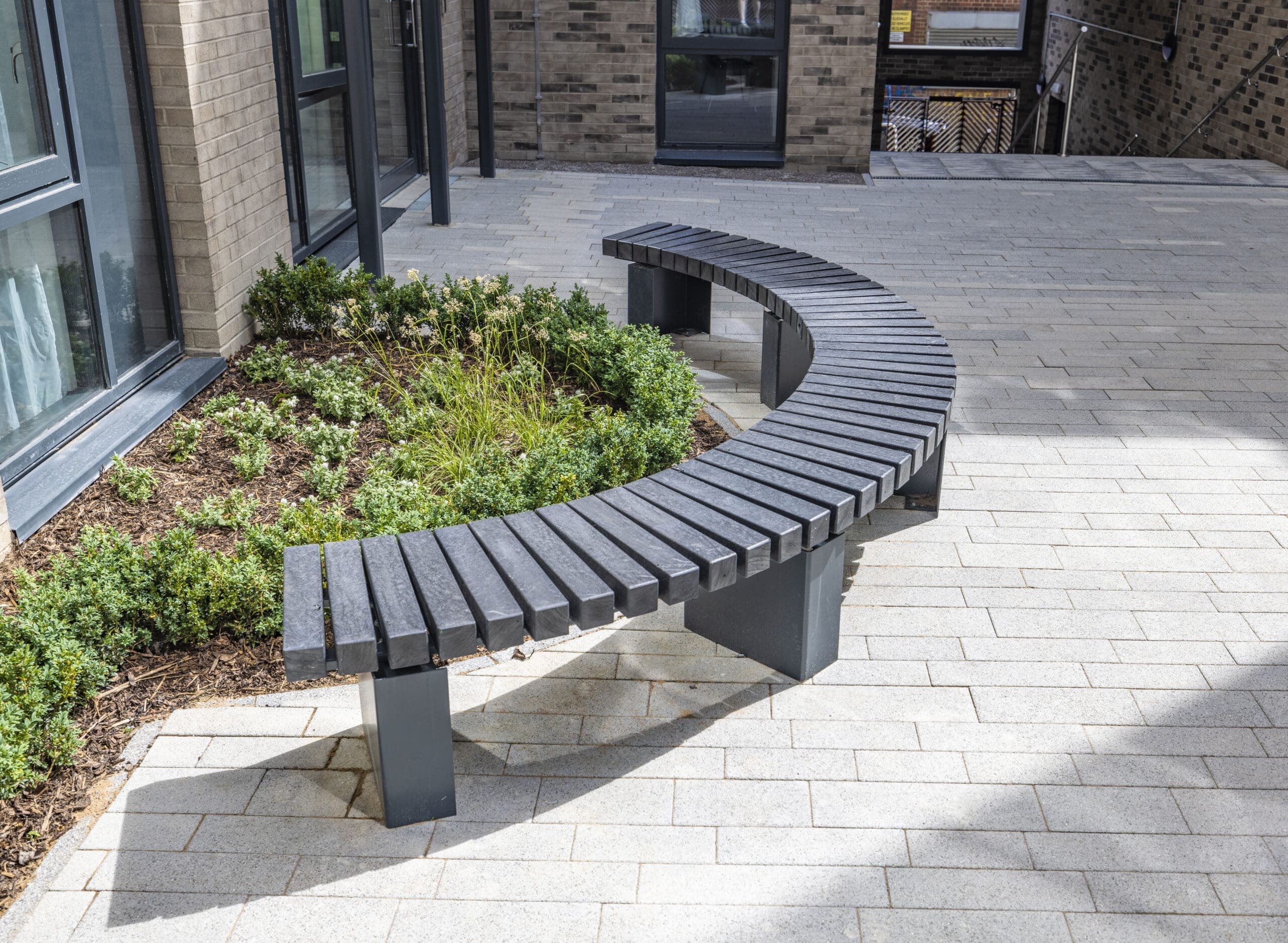 Grey curved bench, outside on a sunny day.