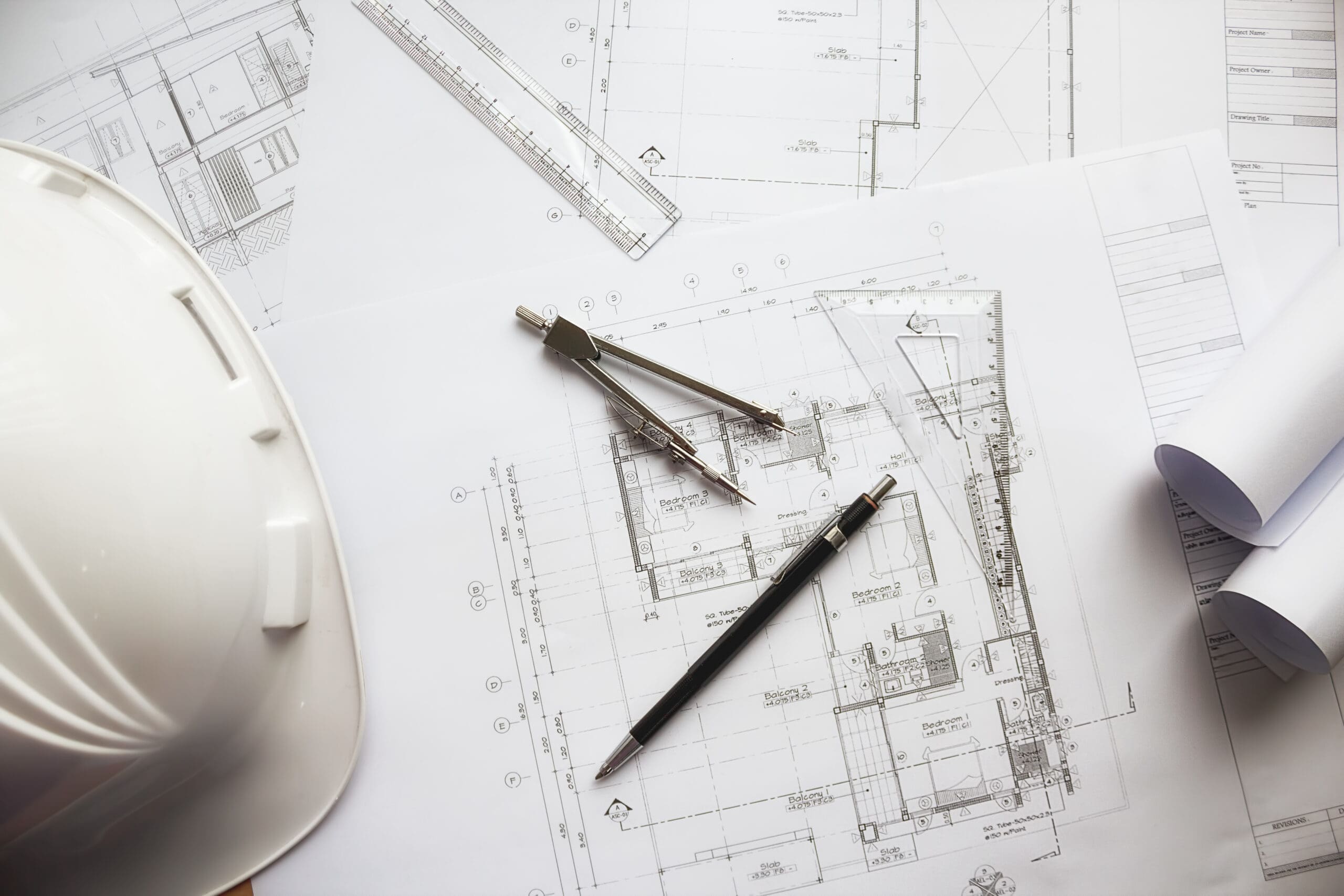 Architect design plans, with a pen and a white hard hat. 